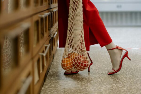 A person in red heels carrying oranges in a mesh bag. Stylish modern shopping scene.