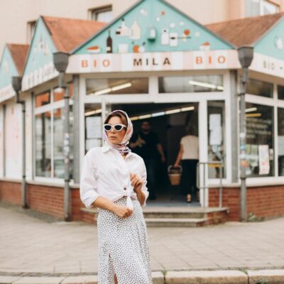 Chic woman with sunglasses poses stylishly outside a modern bio store.