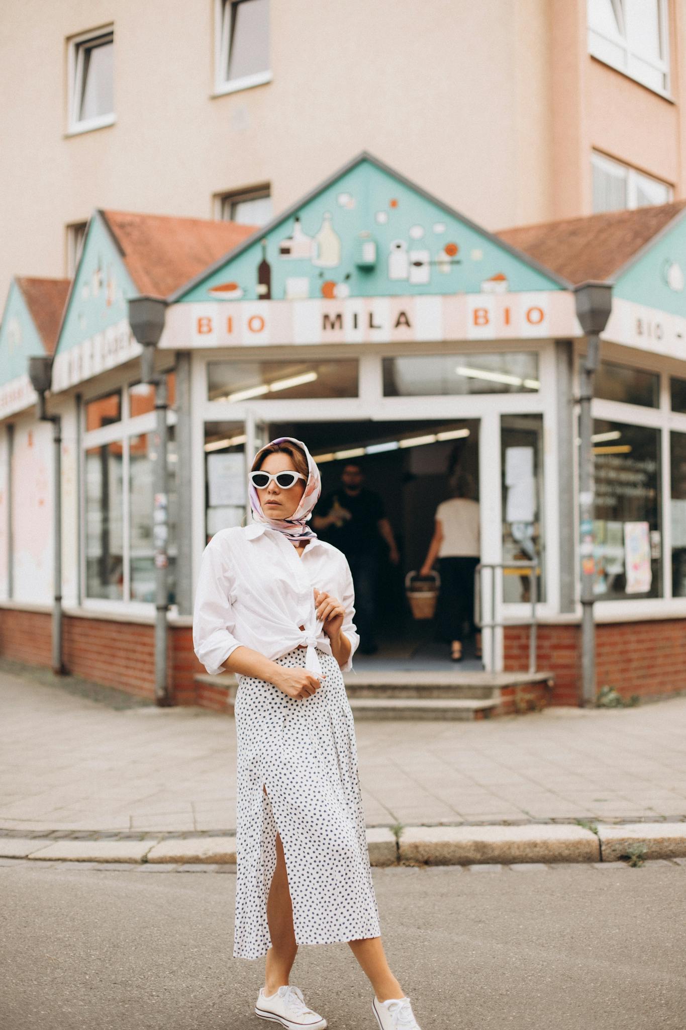 Chic woman with sunglasses poses stylishly outside a modern bio store.