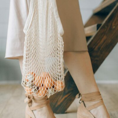 Close-up of a woman in heels carrying a net bag filled with groceries, promoting eco-friendly fashion.