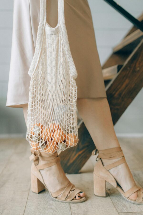 Close-up of a woman in heels carrying a net bag filled with groceries, promoting eco-friendly fashion.