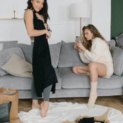 Two women relaxing while trying on new clothing purchases in a cozy living room setting.